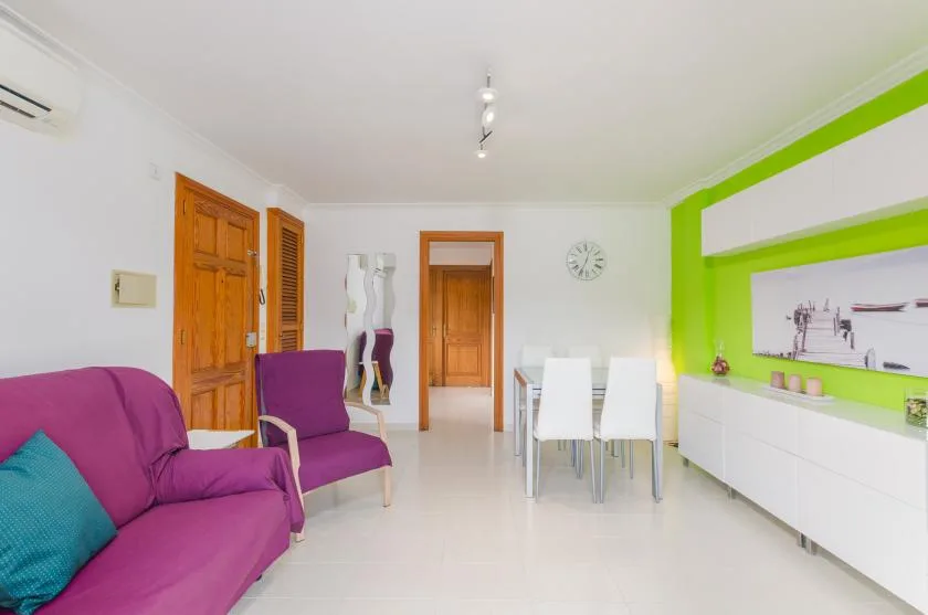 A bright living and dining room with purple seating and white dining chairs.