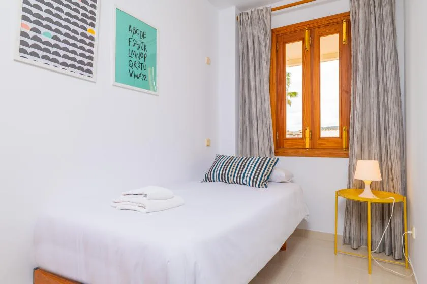 A bright bedroom with a neatly made bed and a wooden-framed window.