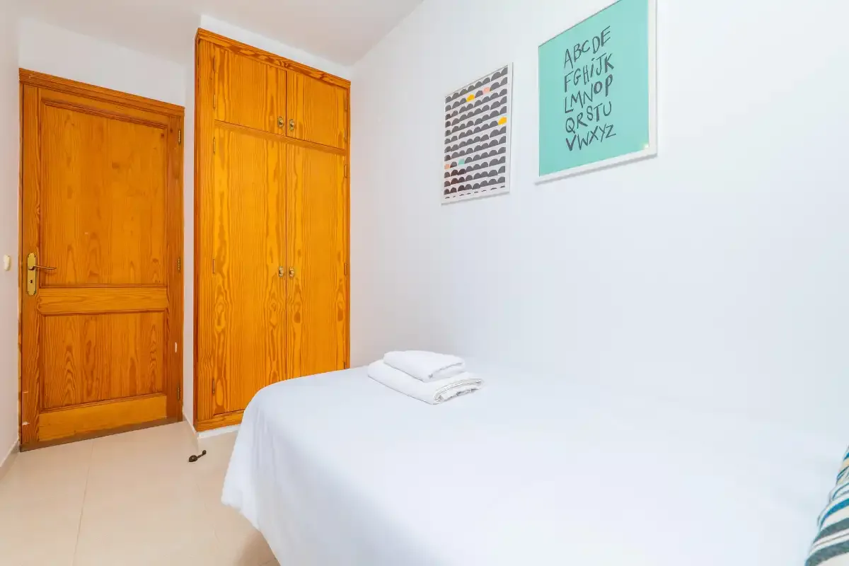 A bedroom with a neatly made bed and wooden storage cabinets.