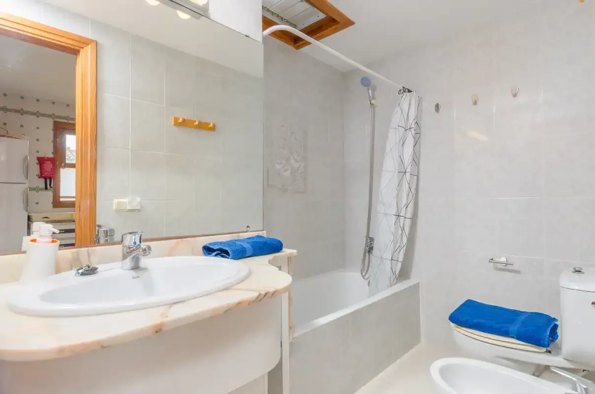 A bright bathroom with a sink, bathtub, and blue towels.