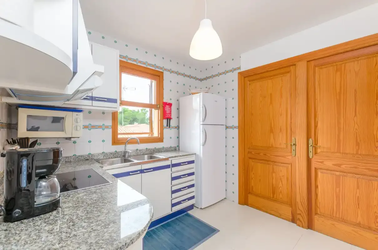 A bright kitchen with a countertop, appliances, and wooden doors.