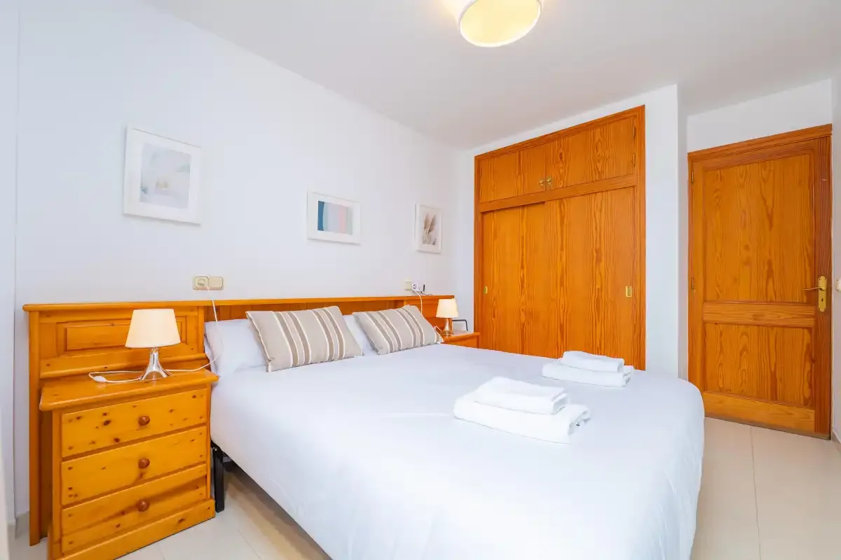 A bright bedroom with a large bed, wooden headboard, and matching wardrobe.