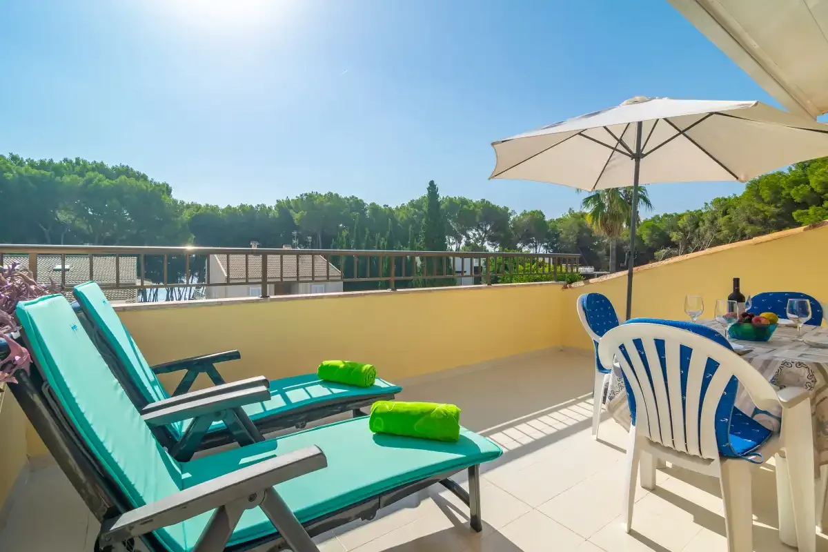 A sunny terrace has turquoise loungers, a dining table, and an open umbrella.