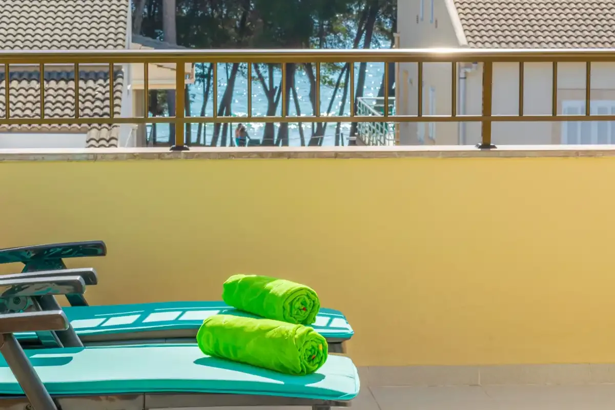A sunlit outdoor terrace with turquoise lounge chairs and a yellow wall.