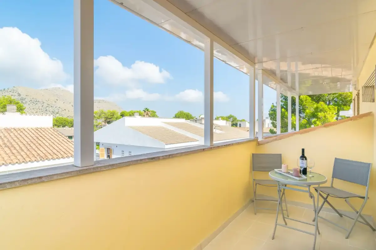 A glazed terrace with a small table and chairs overlooks nearby rooftops.