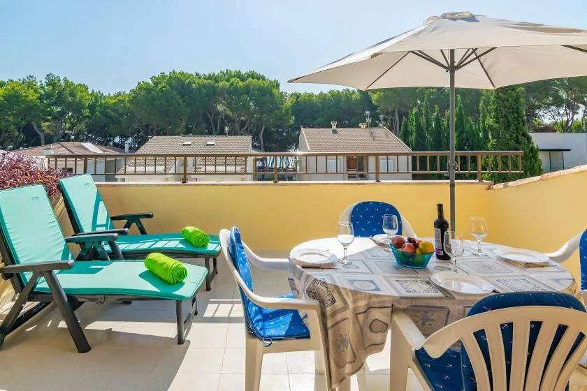 A sunny terrace has outdoor seating and a table set beneath a large umbrella.