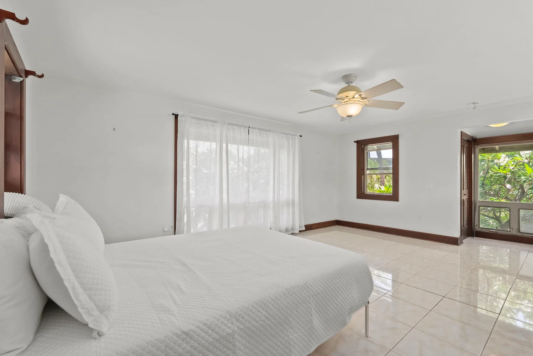 Un dormitorio luminoso con una cama grande, cortinas translúcidas y ventanas con vistas a la vegetación.
