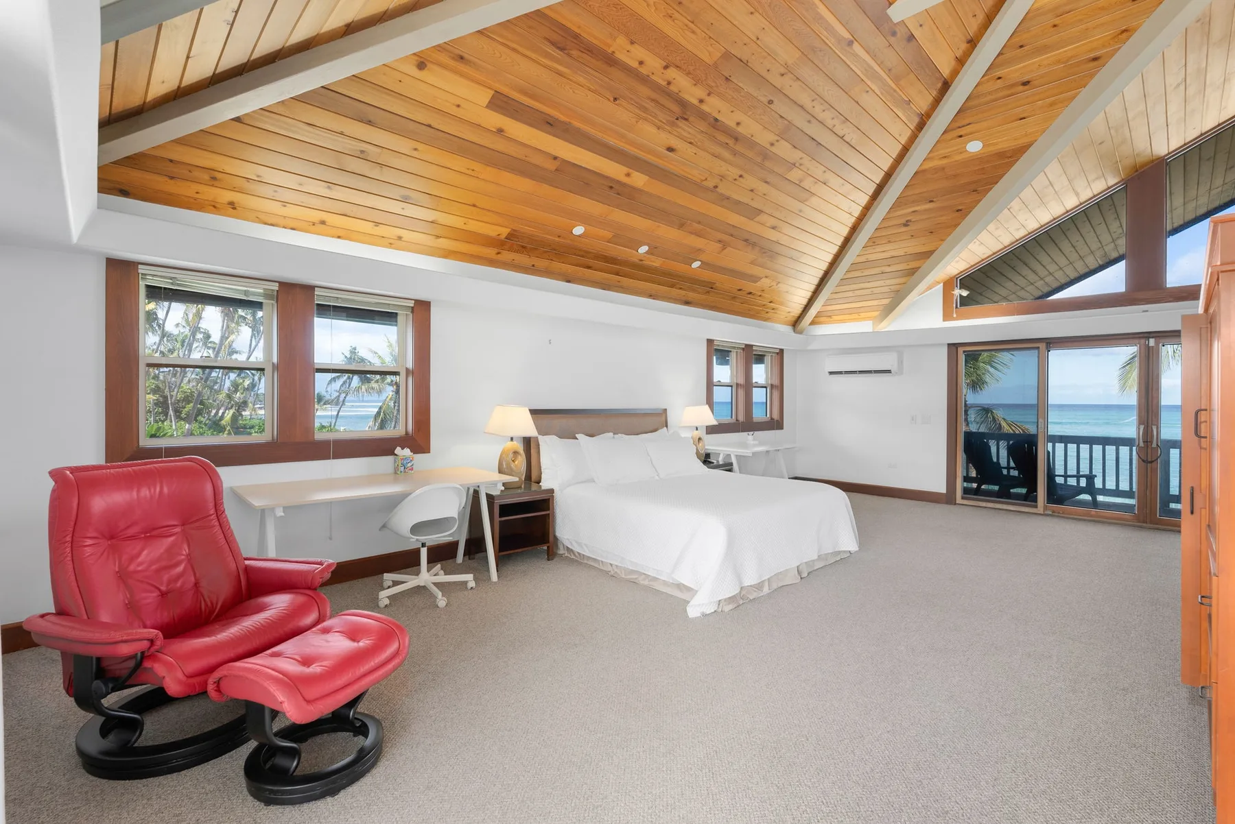 Un dormitorio con una cama, asientos rojos y ventanas con vista al agua.