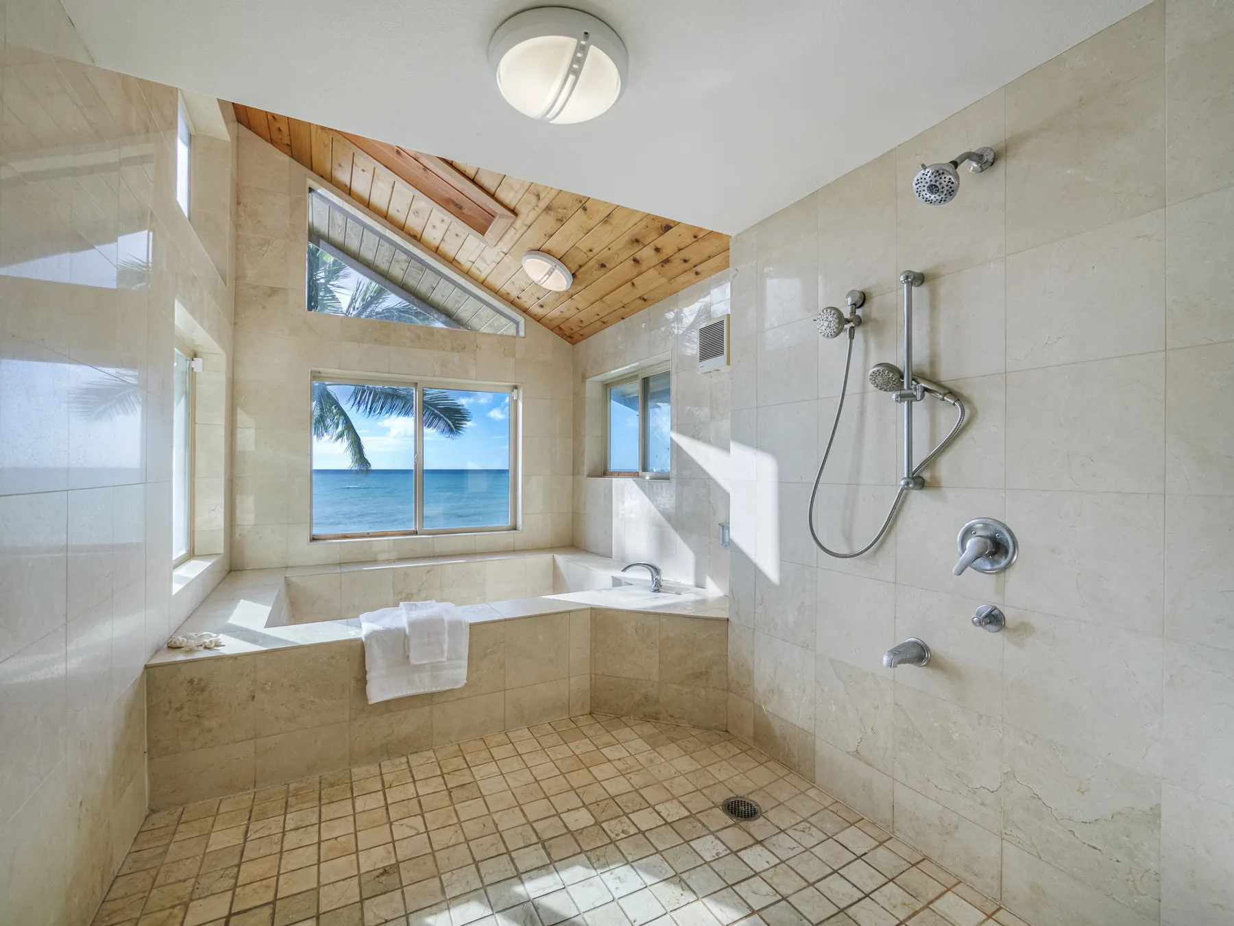 Un baño de azulejos con ducha y una ventana amplia con vista al océano.