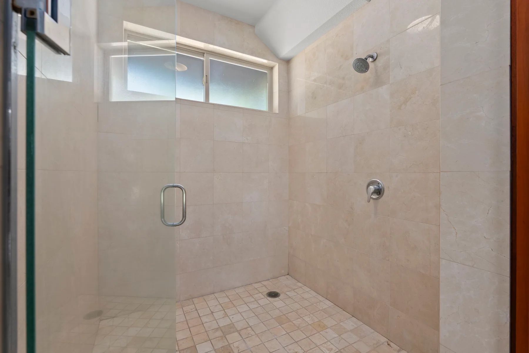 Una ducha revestida de azulejos con una ventana pequeña y accesorios metálicos.