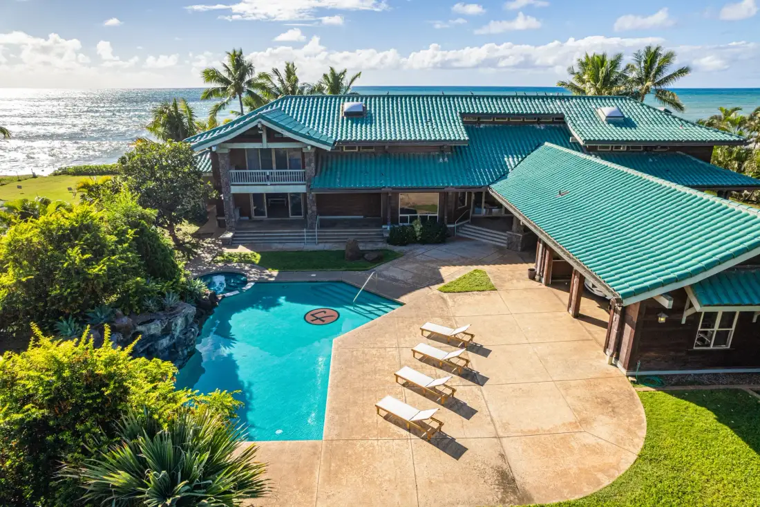 Una casa tropical rodea una piscina junto al océano.