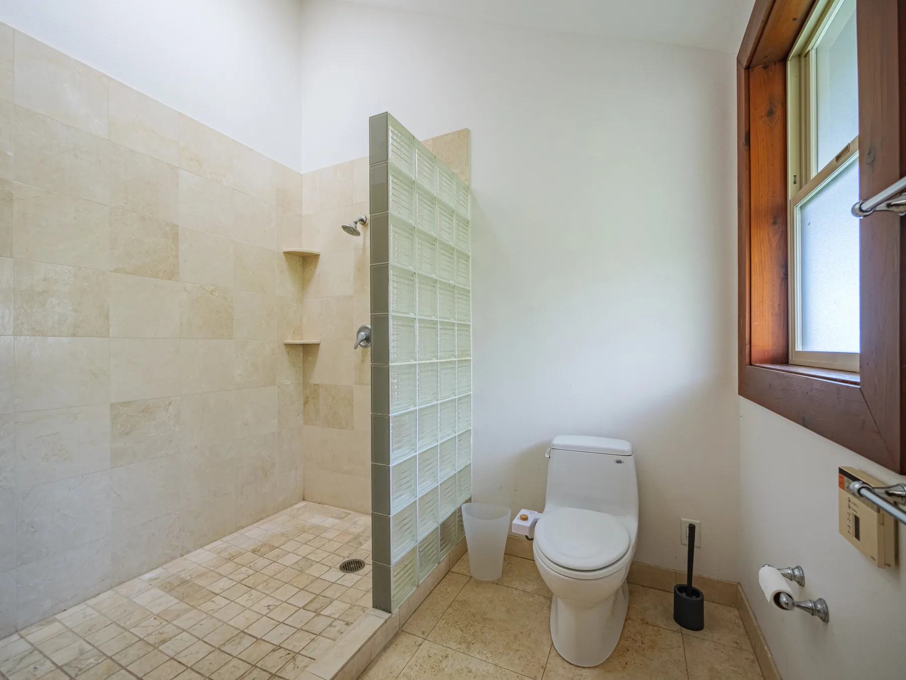 Un baño luminoso con ducha alicatada, inodoro y ventana.