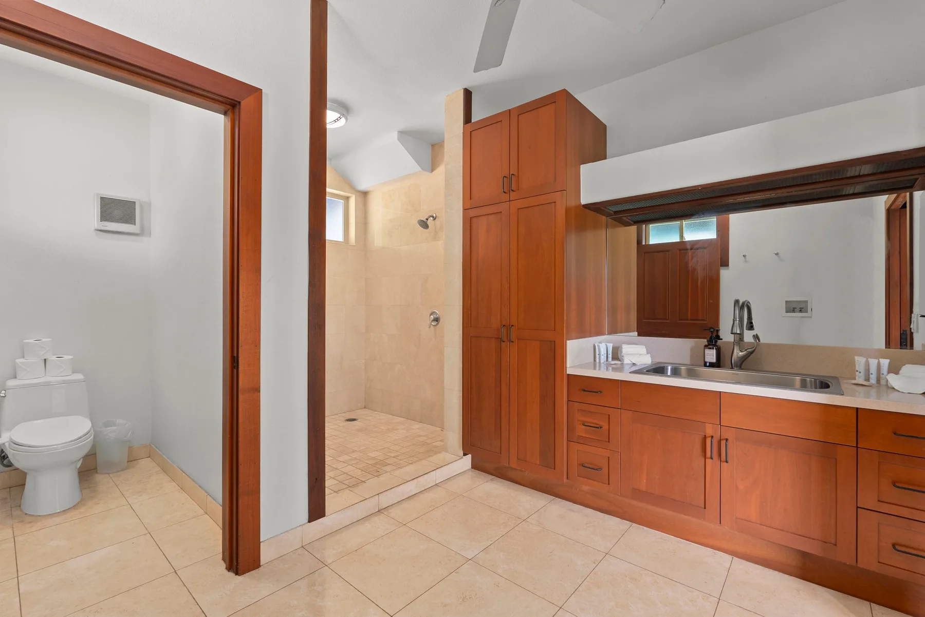 Un baño amplio con ducha, inodoro y un mueble de lavabo largo.