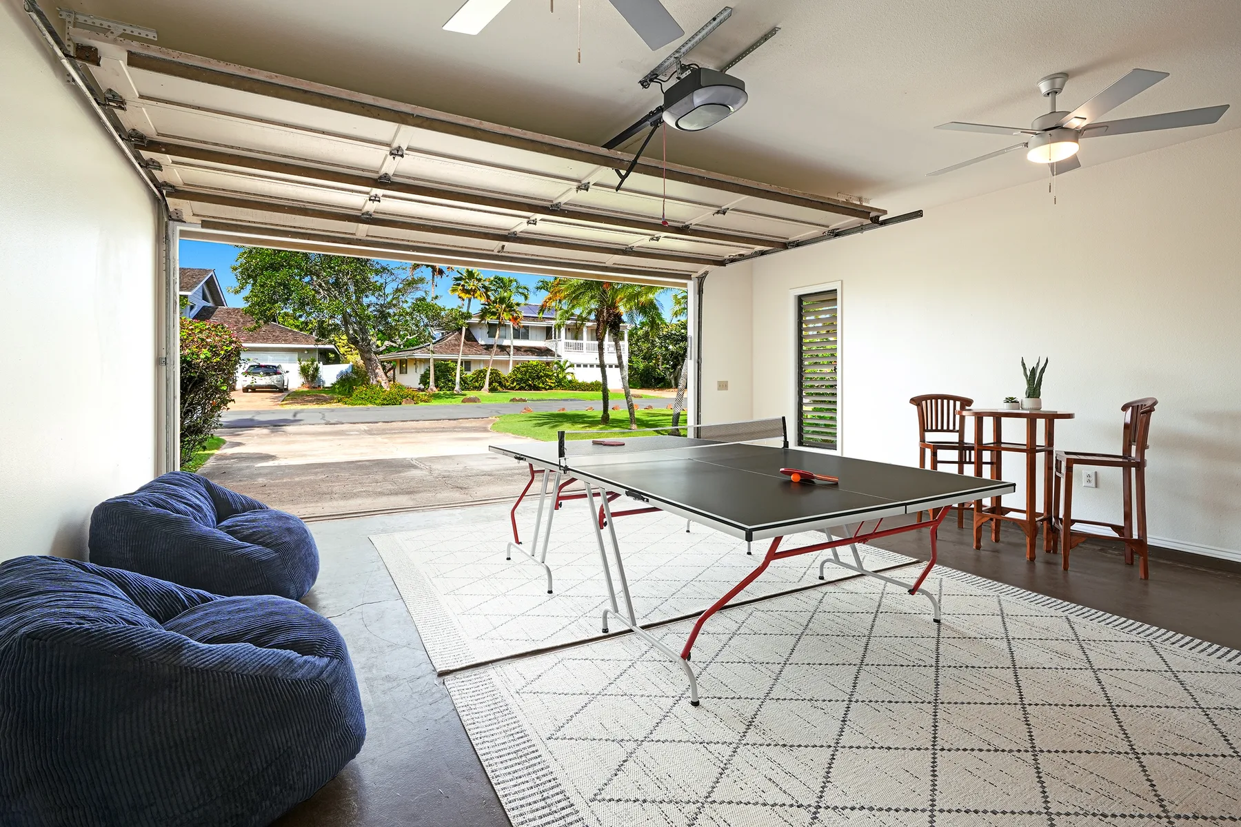 An open garage game area has a ping-pong table, seating, and a tall dining table.