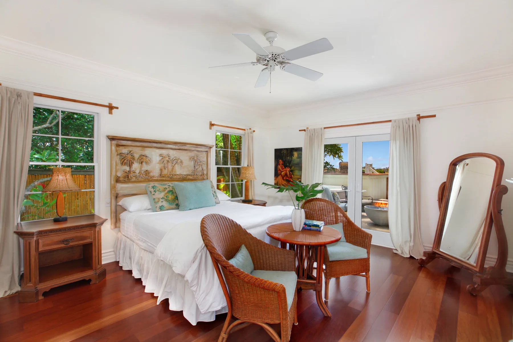 A bright bedroom with a bed, wicker seating, and glass doors opening to a balcony.