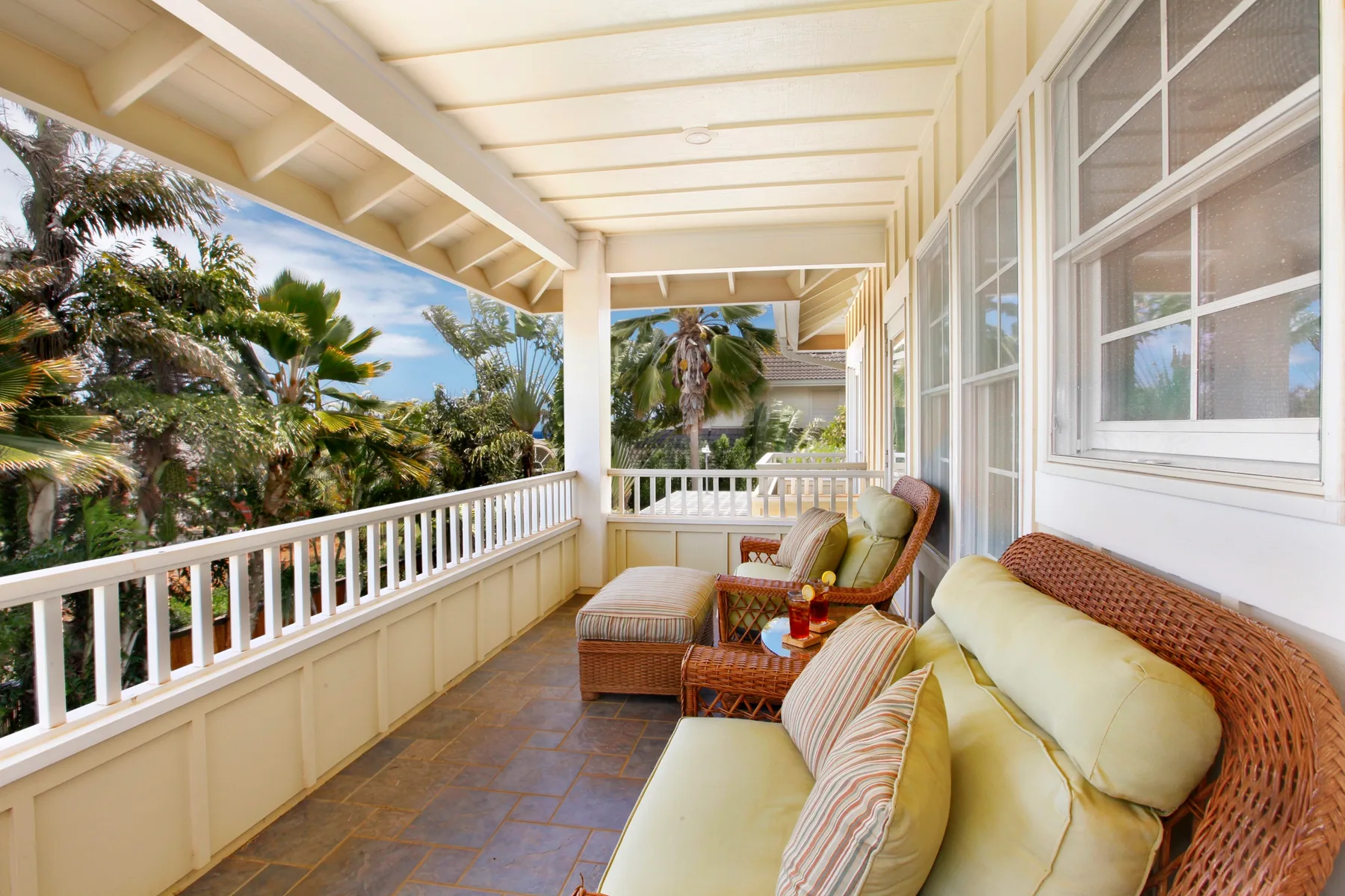 A covered porch with cushioned seating and tropical plants visible beyond the railing.