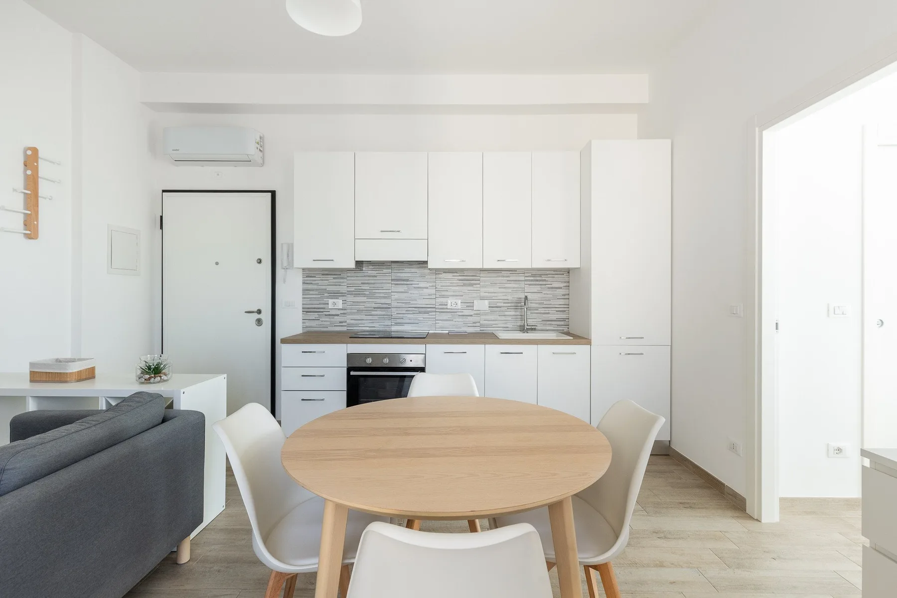 Una cocina luminosa con comedor, armarios blancos y una mesa redonda de madera.