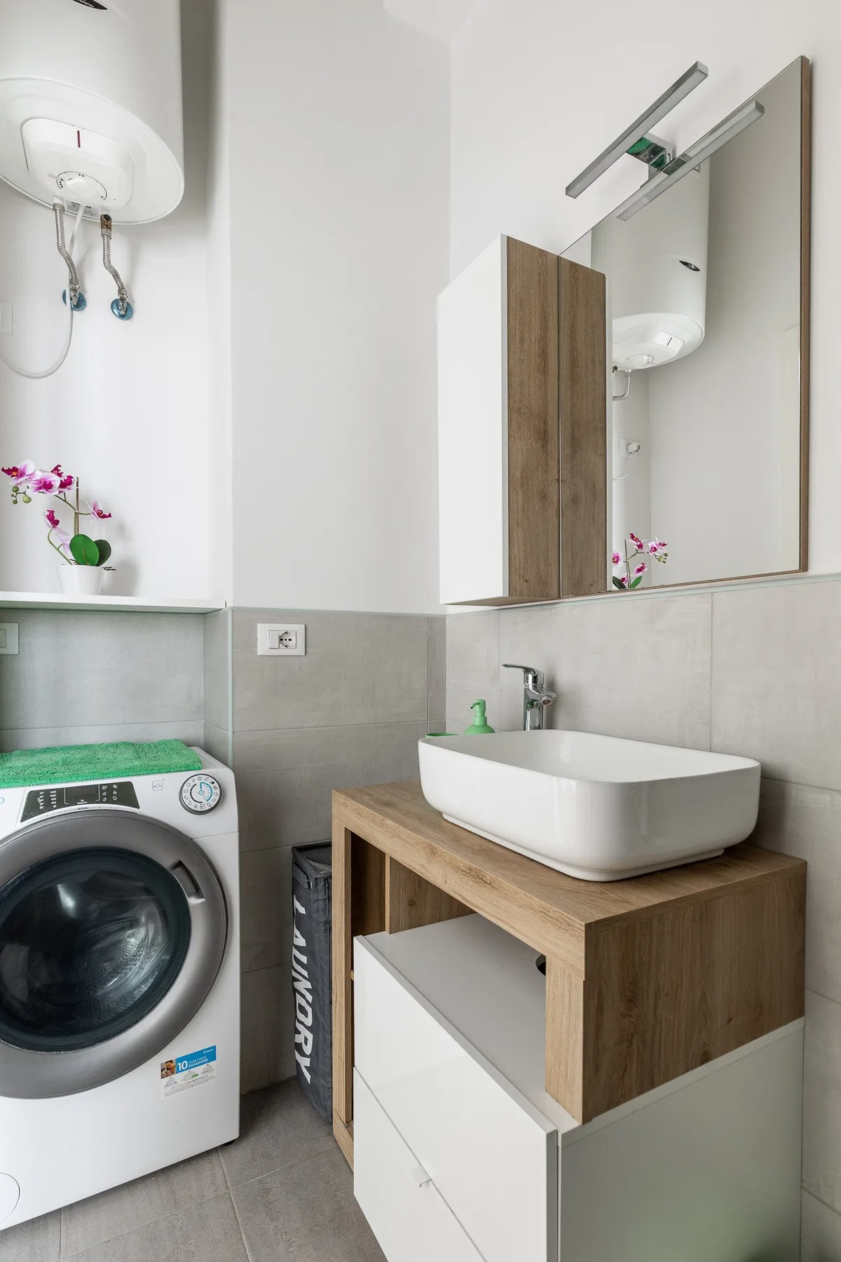 Un mueble de baño con lavabo y espejo está junto a una lavadora.