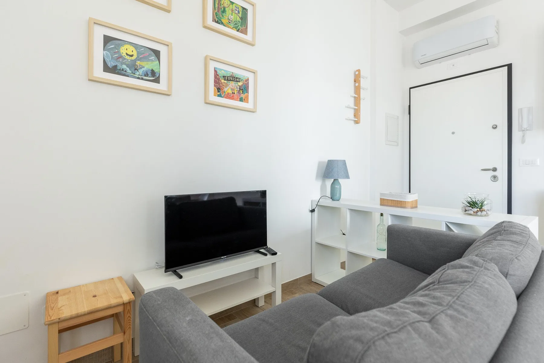 Una sala luminosa con asientos grises, un televisor y cuadros en la pared.
