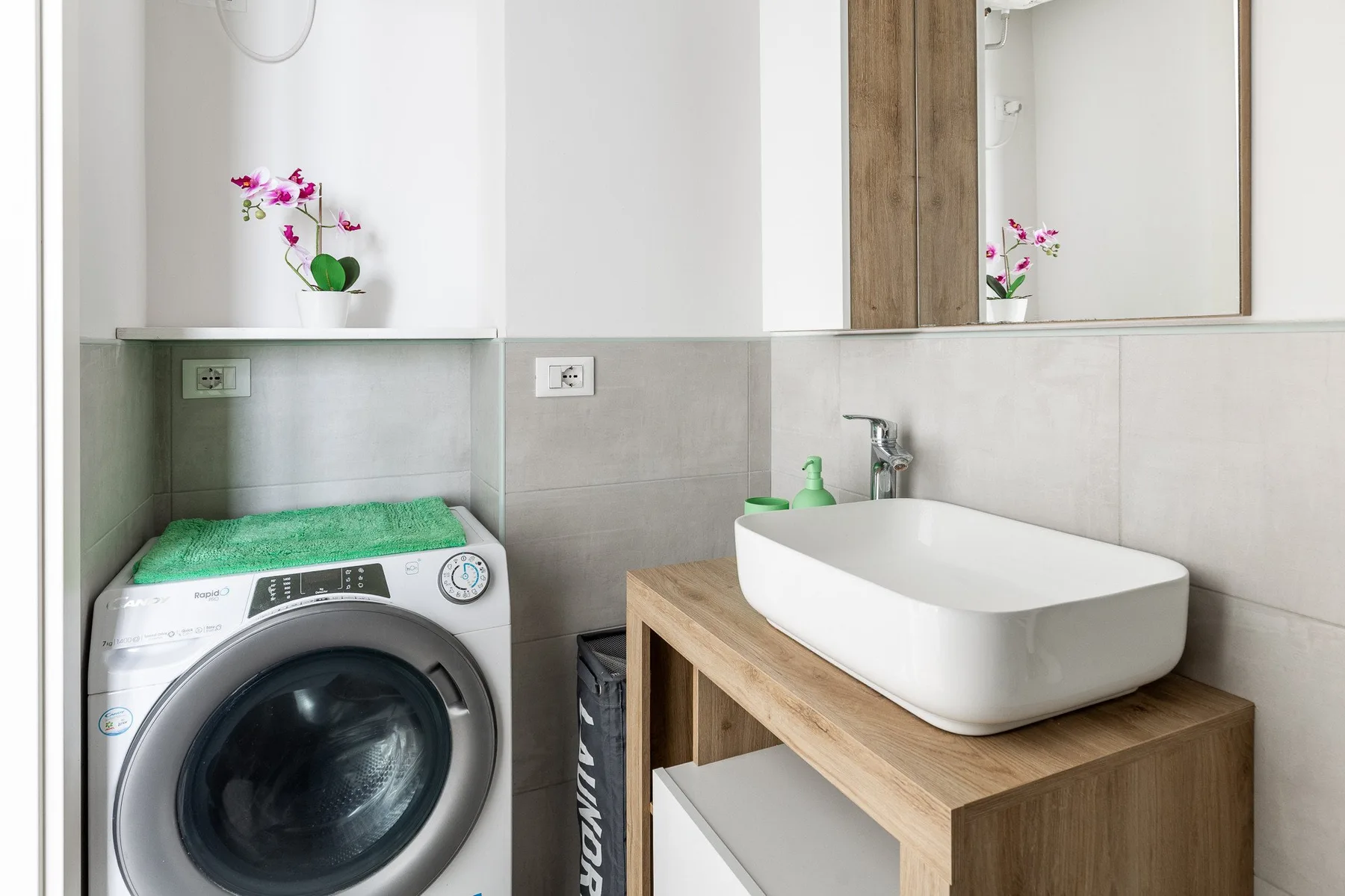 Un baño con una lavadora junto a un lavabo sobre un mueble de madera.