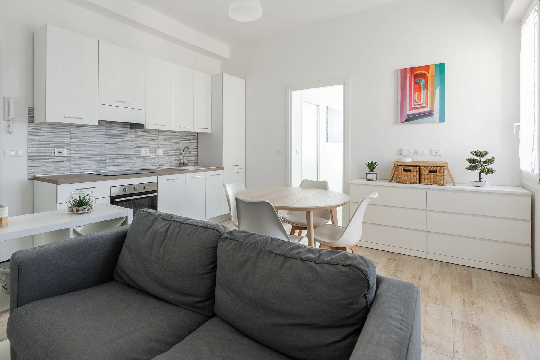 Una luminosa sala-comedor de concepto abierto con cocina y asientos grises.