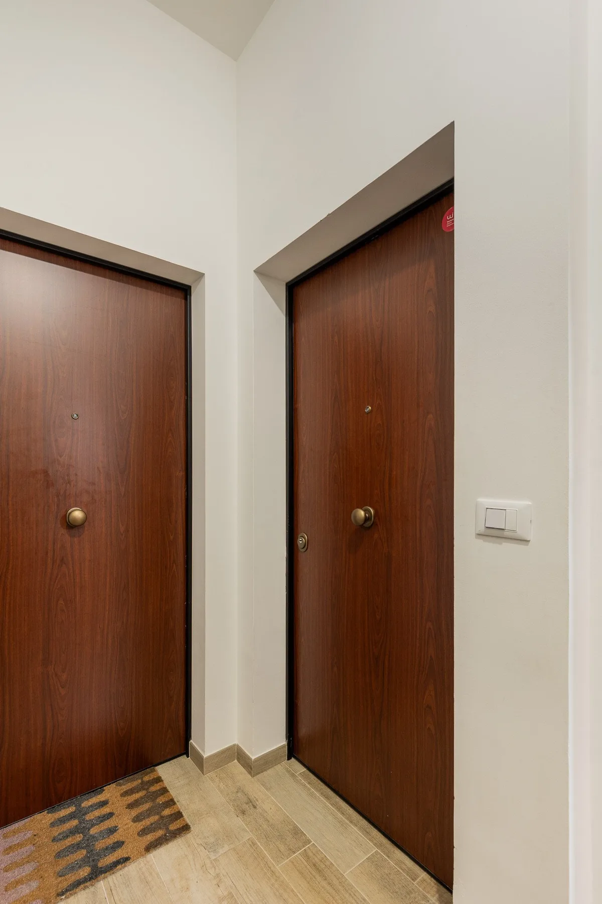 Un pasillo interior con dos puertas de madera oscura y suelo de baldosas.