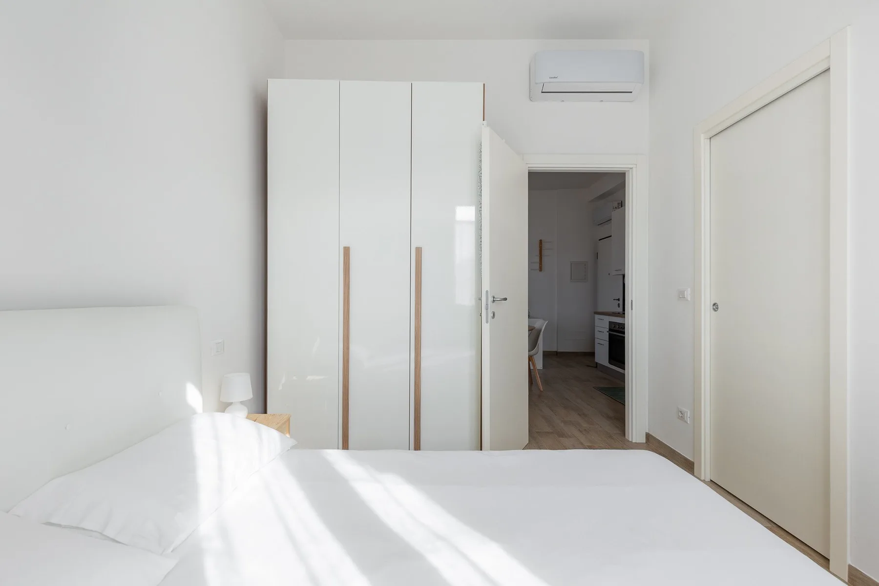 Un dormitorio luminoso con una cama blanca y un armario alto.