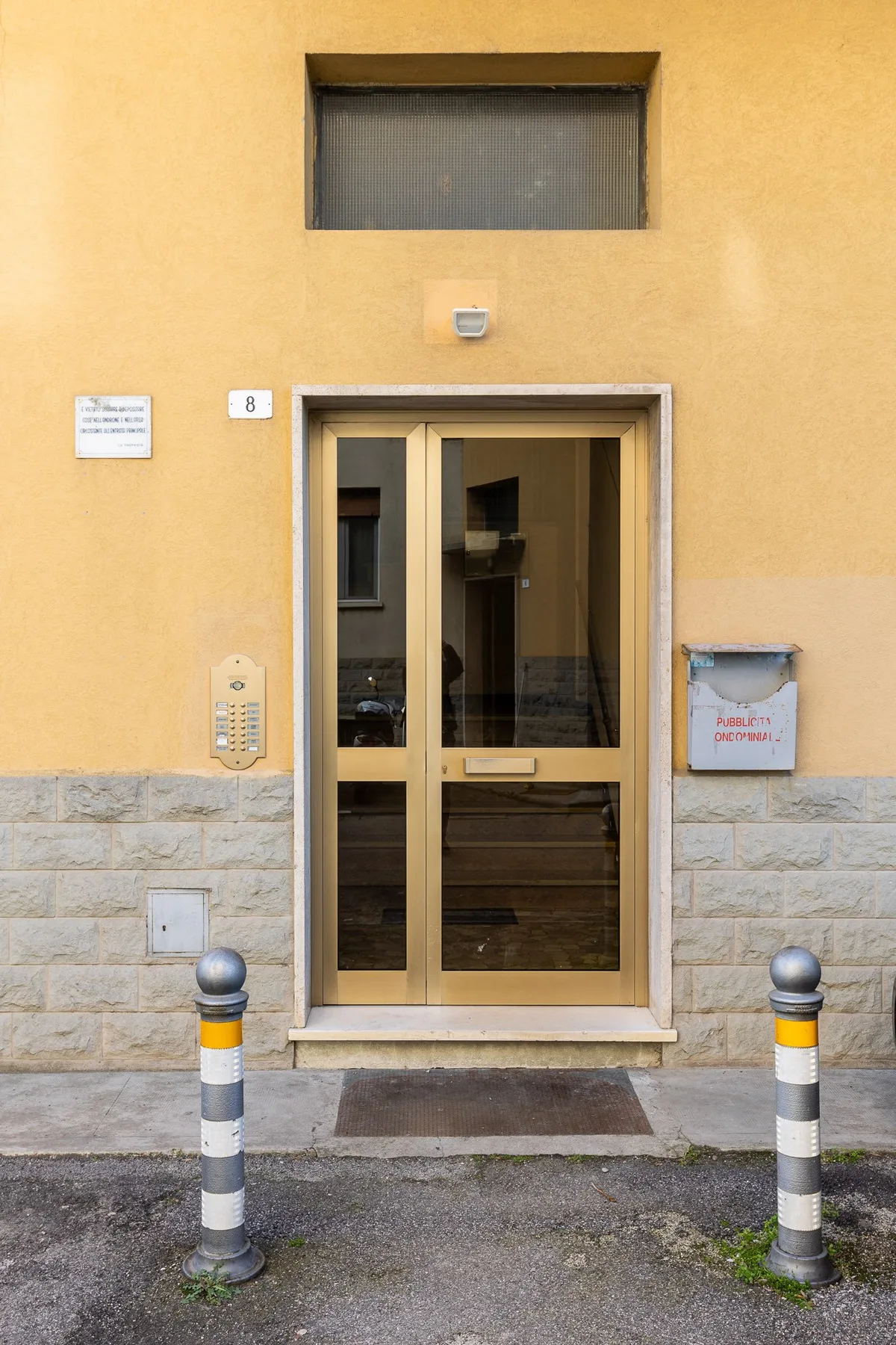 Una puerta de entrada de vidrio está en una pared exterior amarilla sobre una base de piedra.
