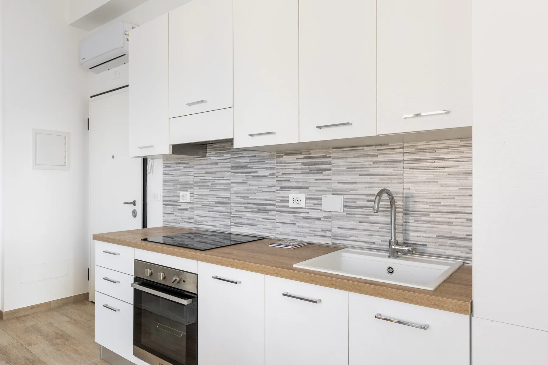 Una cocina moderna y luminosa con gabinetes blancos, una placa de cocción y un fregadero.