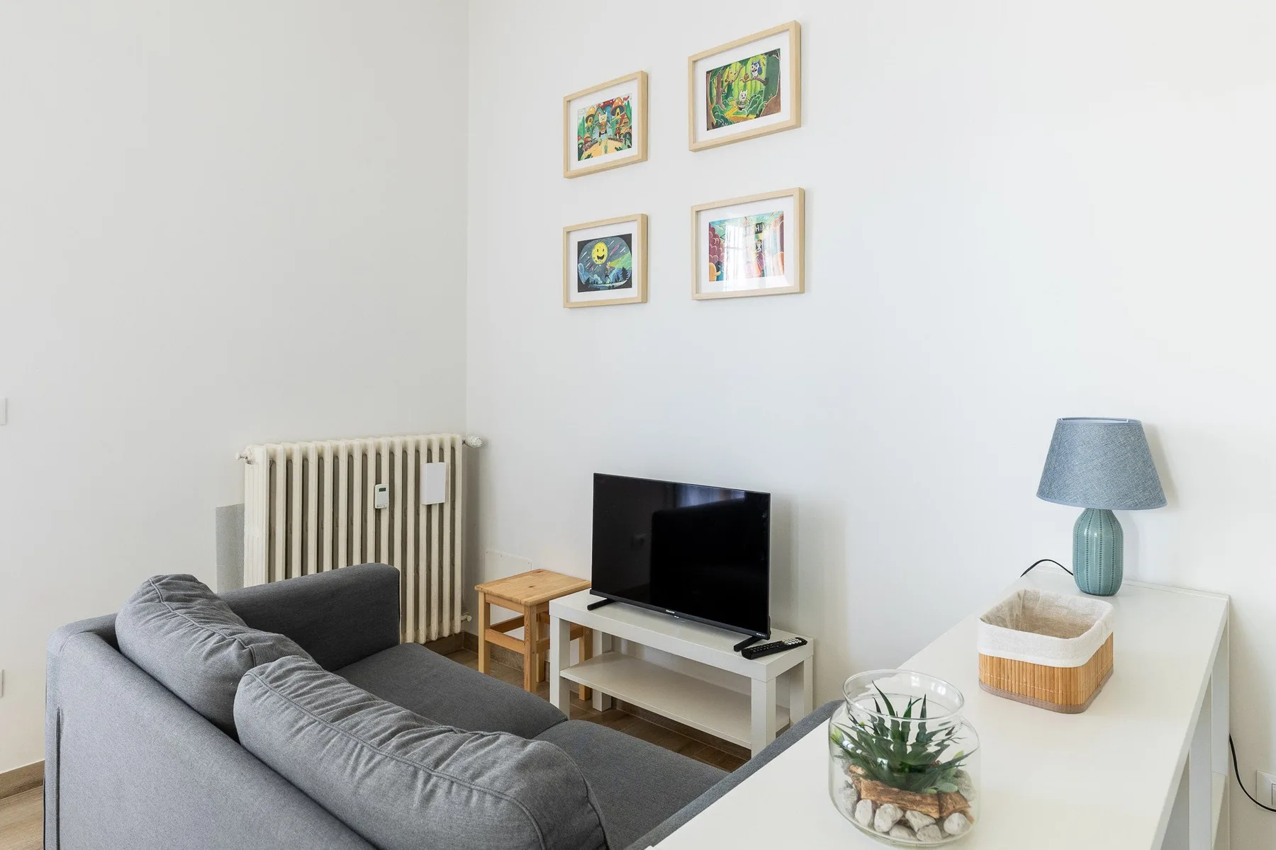 Una sala de estar con un sofá gris, un televisor y cuadros en la pared.
