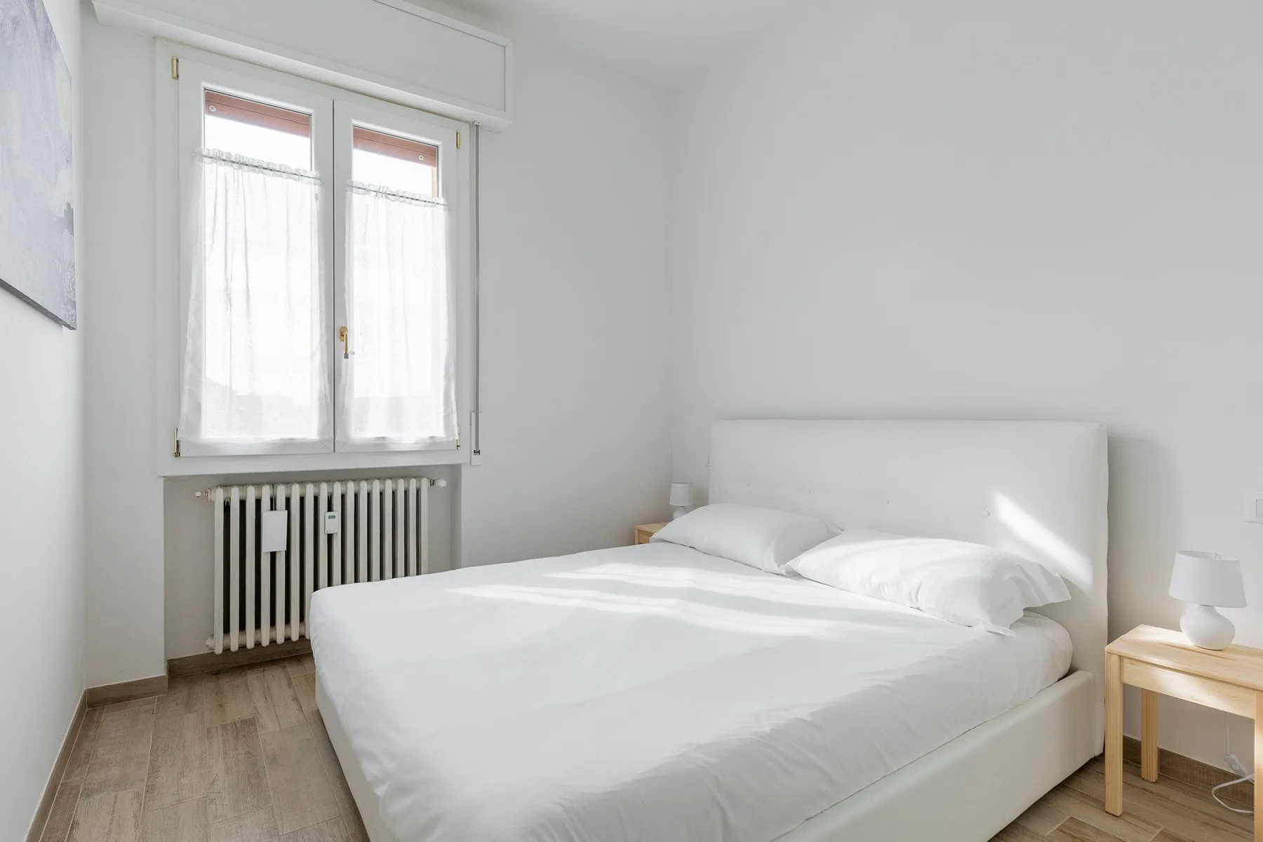 Un dormitorio luminoso con una cama bien tendida junto a una ventana con cortinas.