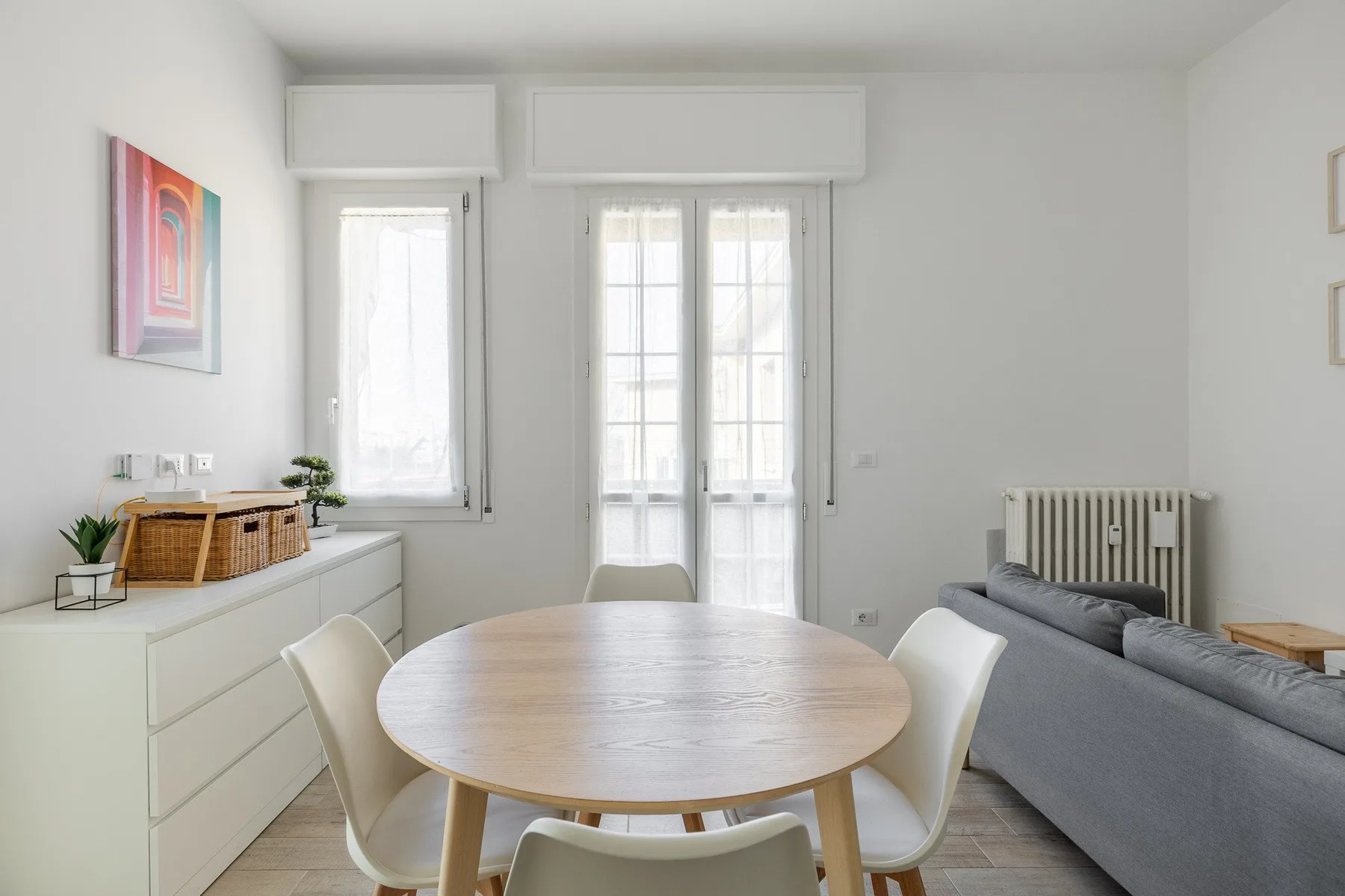 Una luminosa zona de comedor y estar con una mesa redonda junto a un sofá gris.