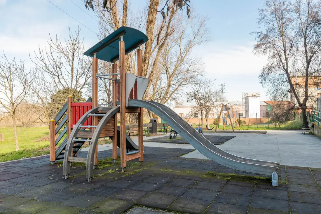 Un parque infantil con tobogán y estructura para trepar está junto a una zona pavimentada.