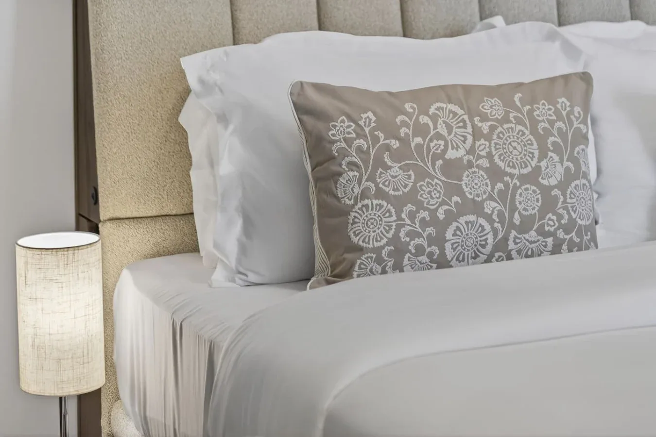 A neatly made bed with white bedding and a patterned decorative pillow.