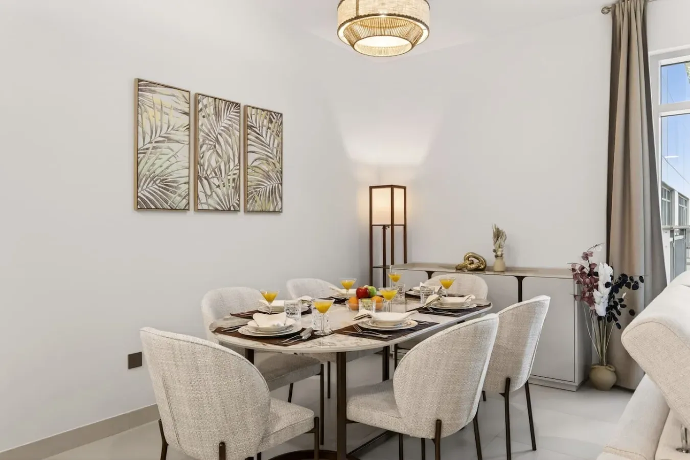 A bright dining area has a table set for a meal and upholstered seating.