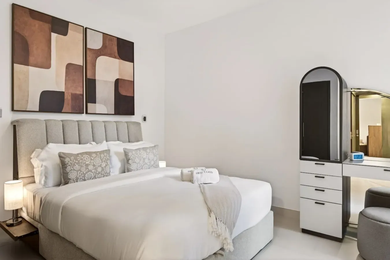 A bedroom with a neatly made bed and abstract artwork above the headboard.