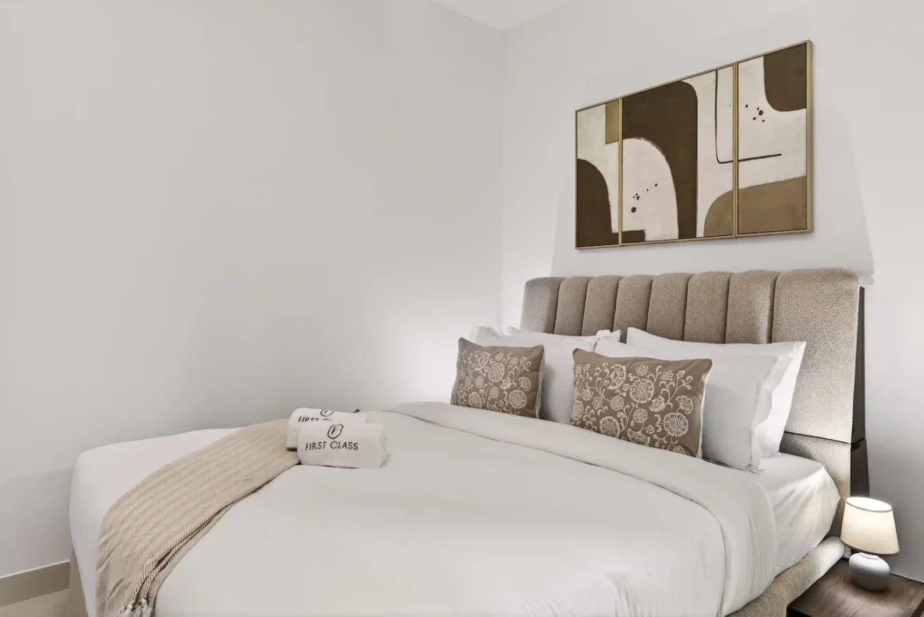 A bedroom with a neatly made bed and abstract artwork above the headboard.