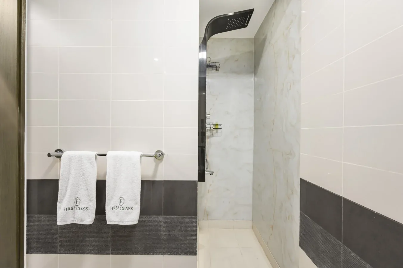 A tiled bathroom shower area with white towels hanging on a rail.