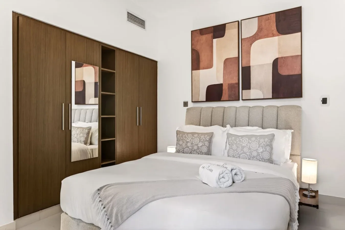 A bedroom with a neatly made bed and abstract artwork above the headboard.