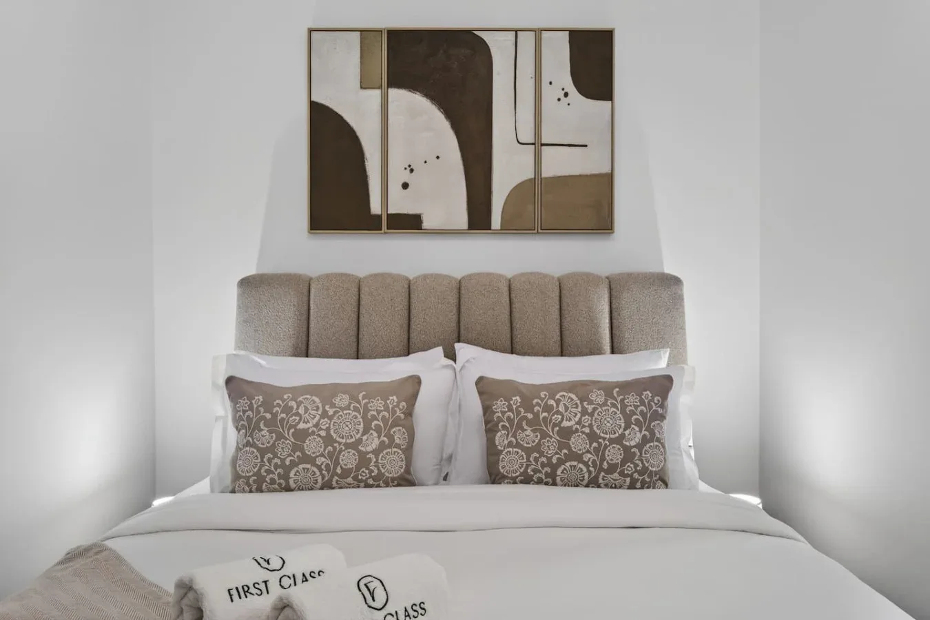 A bedroom with a bed, patterned pillows, and abstract artwork above the headboard.