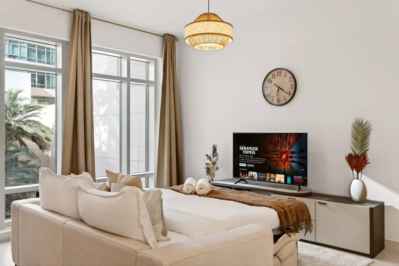 A bright bedroom with a large bed, tall windows, and a television.