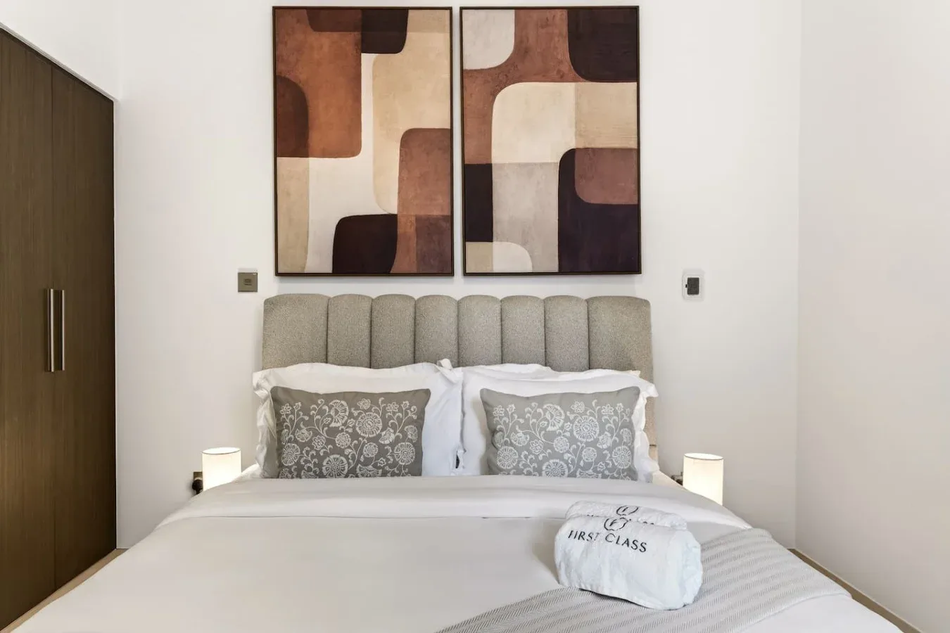 A bedroom with a neatly made bed and abstract artwork above the headboard.