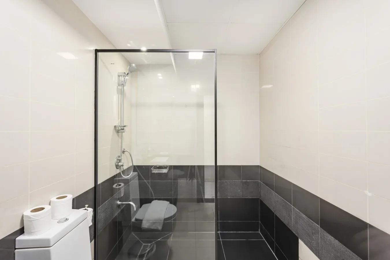 A tiled bathroom with a glass shower and dark wall tiles.