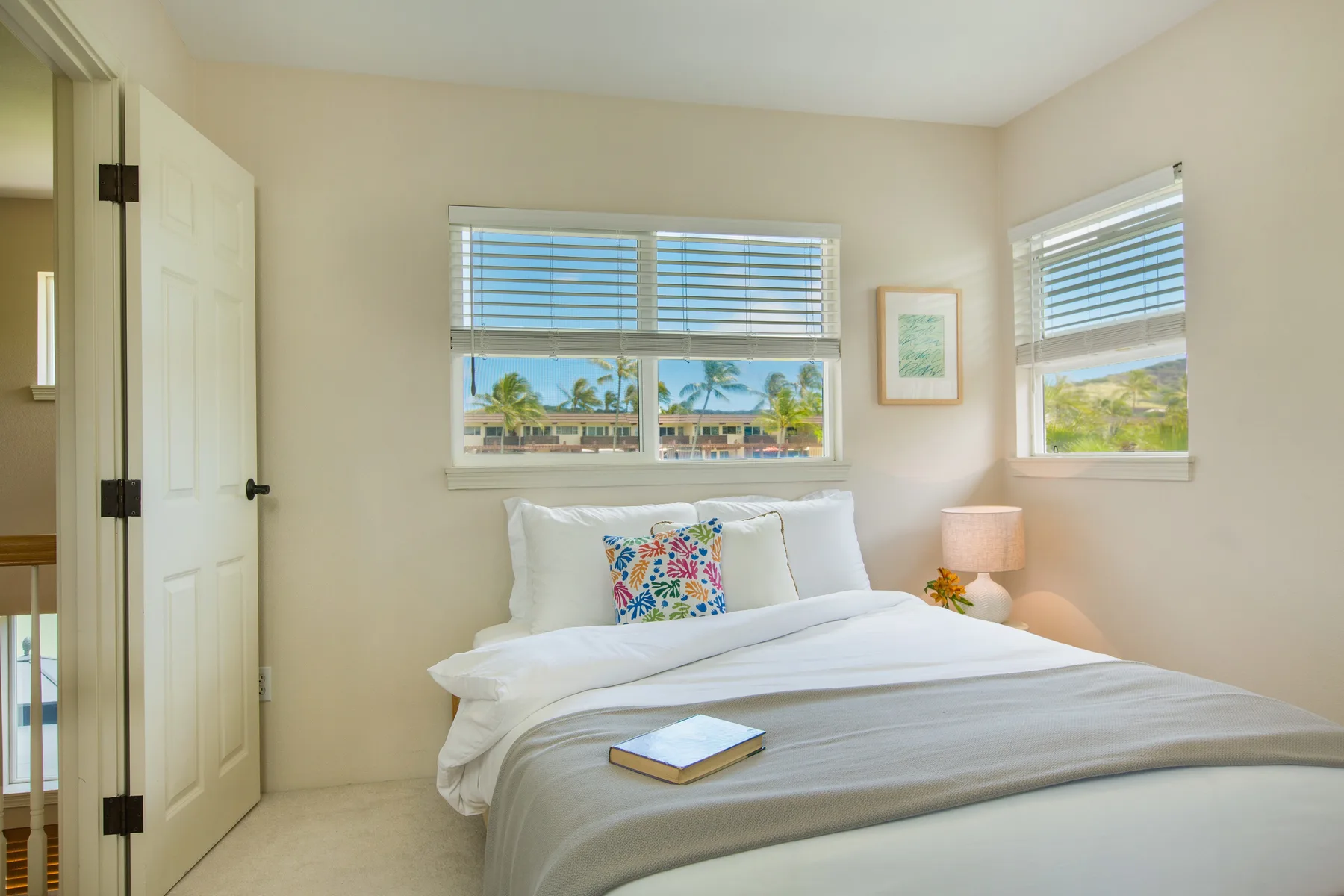 A bedroom with a neatly made bed beneath two windows.