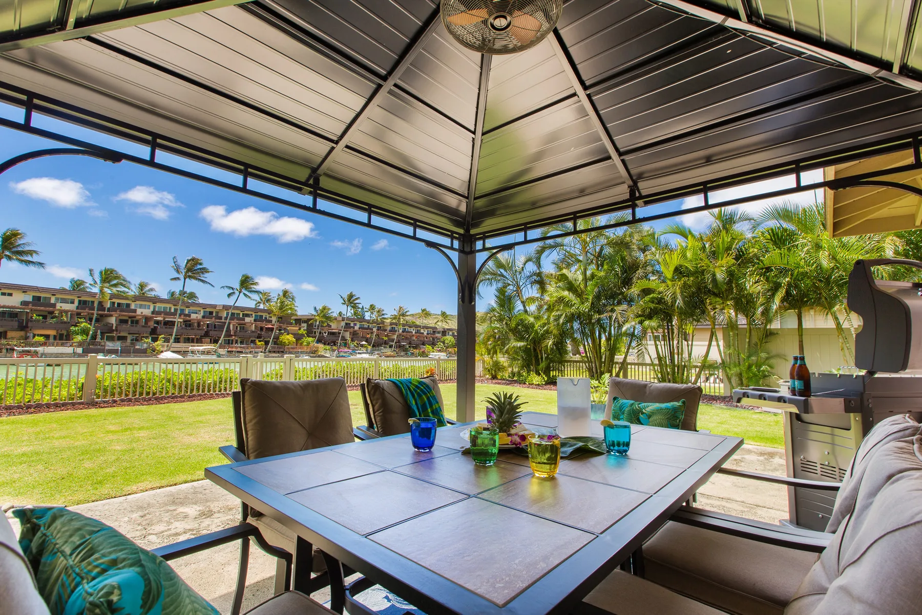 A covered outdoor dining area overlooks a grassy lawn and palm trees.
