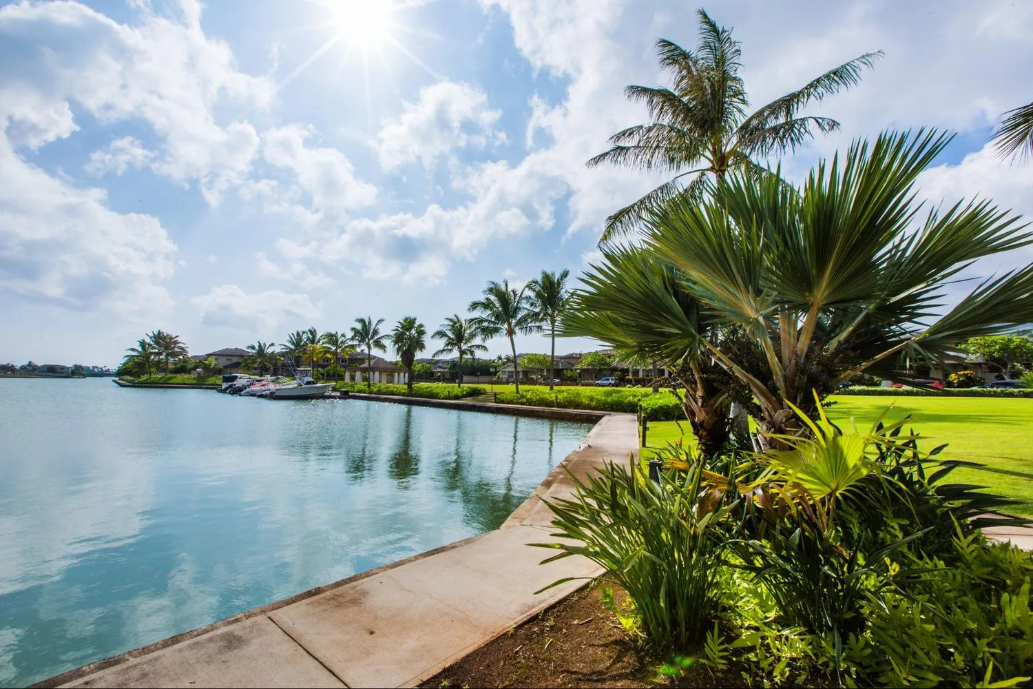 A landscaped waterfront borders calm water beneath a bright, cloudy sky.