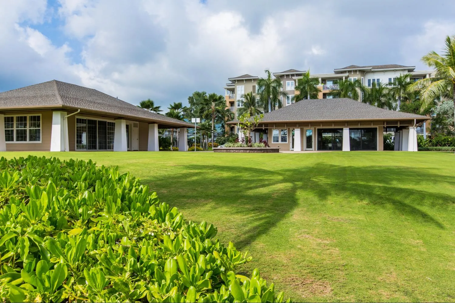 A landscaped lawn with low buildings and palm trees beneath a cloudy sky.