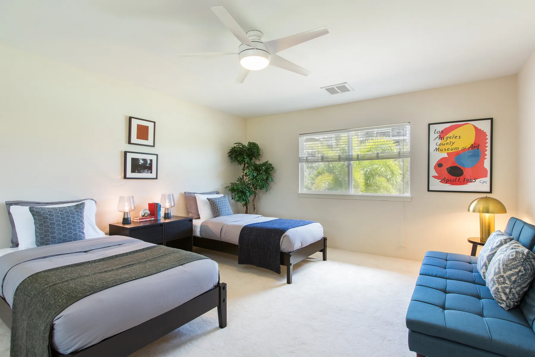 A bedroom with two beds, a window, and blue seating.