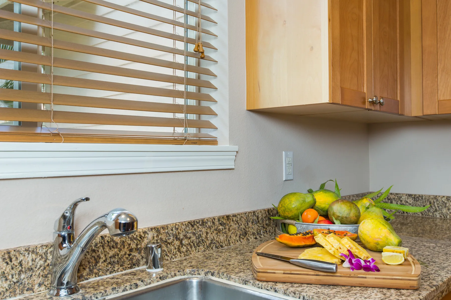 A kitchen counter holds a cutting board with fruit beside the sink.