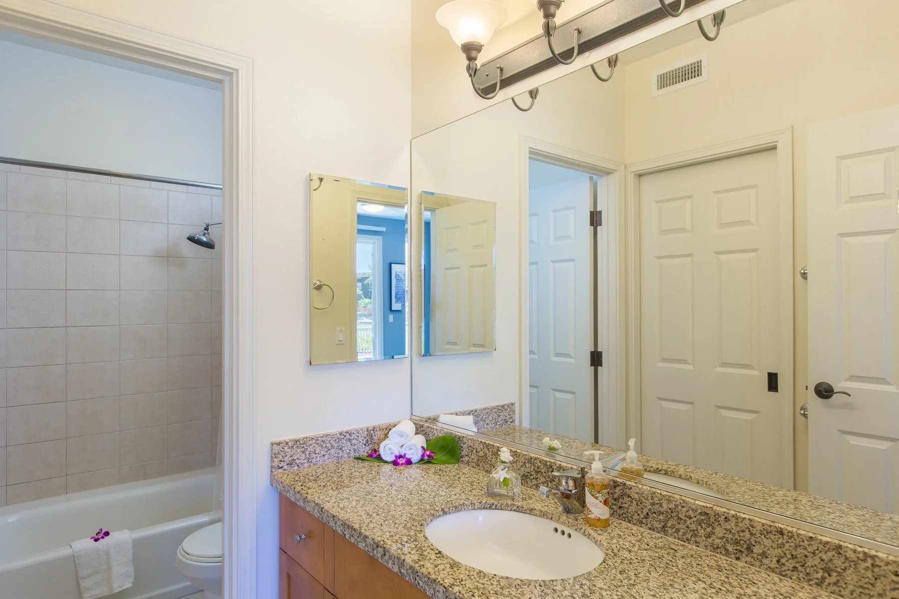 A bathroom vanity with a sink and large mirror beside a tiled shower.